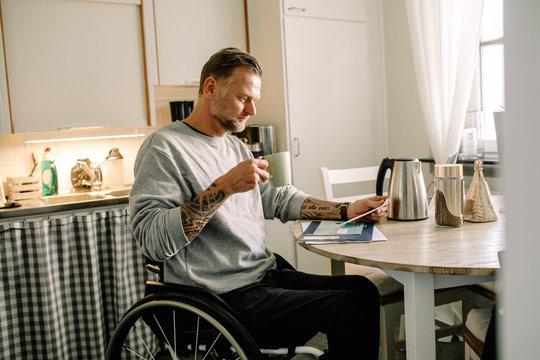 Bearded man in wheelchair reading mail at home