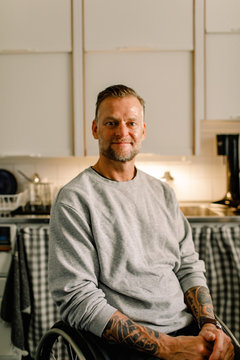 Portrait of confident smiling disabled man sitting on wheelchair in kitchen at home
