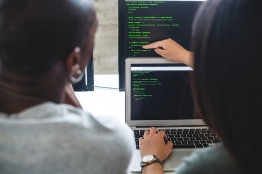 Rear view of female entrepreneur pointing at codes on computer monitor to male hacker in office