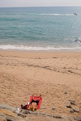 Fototapeta na wymiar Domir ao sol na areia da praia a ouvir rádio e com chapéu de palha