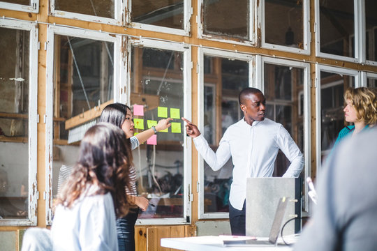 Serious creative professionals pointing at adhesive notes while discussing with team in office