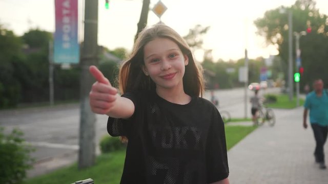 Portrait young happy teenager girl gesturing thumbs up in the street cheerful consumer cute alone sign beautiful good hand joyful fun friendly behavior crowd close up slow motion