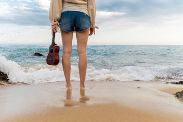 Woman with ukulele standing in front of the sea, partial view