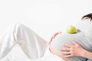 Part of pregnant woman with green apple on the belly. Healthy eating concept with copy space