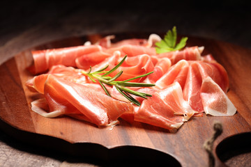 Italian prosciutto crudo or jamon with rosemary. Raw ham on wooden board