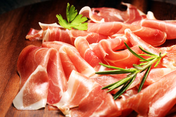 Italian prosciutto crudo or jamon with rosemary. Raw ham on wooden board
