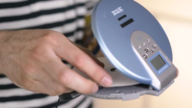 Using a portable CD player by inserting a compact disk to listen to music.