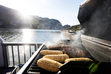 Summer meal of corn on the cob and steak grilled on barbecue at lake
