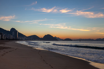 Fototapeta na wymiar Smooth sand beach left by the ocean waves at early morning sunrise on Copacabana in Rio de Janeiro with the Sugarloaf mountain in the background