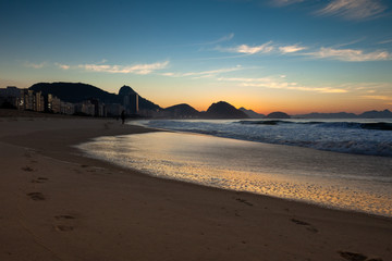 Early morning Copacabana beach in Rio de Janeiro with the Sugarloaf mountain in the background just before sunrise with deep orange and blue colours in the sky