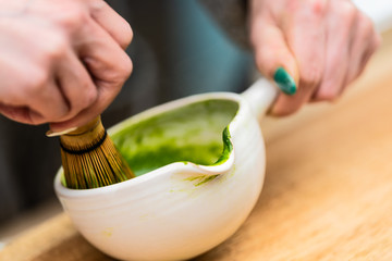 Closeup of woman holding Japanese tea cup teapot pot and whisk on table making, stirring and preparing koicha matcha hot drink