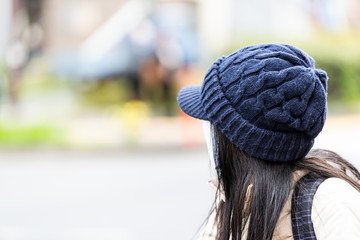 Young Japanese Asian woman standing on street looking back dressed in hat and mask with blurred urban background