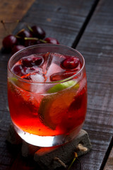 cherry and lime cocktail on a wooden floor with garnish