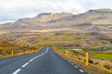 Road highway 31 in Iceland on golden circle with straight street asphalt by autumn landscape on cloudy day and car far by farm fields