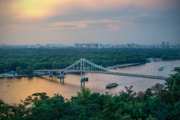 Parkovy (Pedestrian) Bridge at sunset, seen from the Khreshchatyy Park with ships passing beneath, Kiev, Ukraine