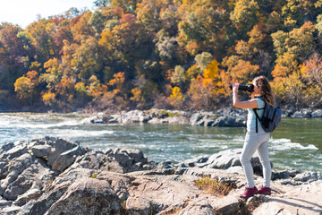 Young woman photographer taking photo picture with camera of view of Potomac river in Great Falls with autumn colorful foliage in Maryland
