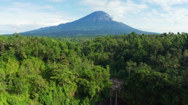 Exotic aerial view of Tumpak Sewu waterfall with green forest and Mount Semeru background. Shot in 4k resolution from a drone flying backwards