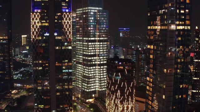JAKARTA, Indonesia - June 26, 2019: Aerial landscape of modern office buildings with beautiful night lights in business district. Shot in 4k resolution from a drone flying from right to left