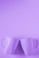 Purple coffee mugs on purple background clinking in cheers with empty copy space