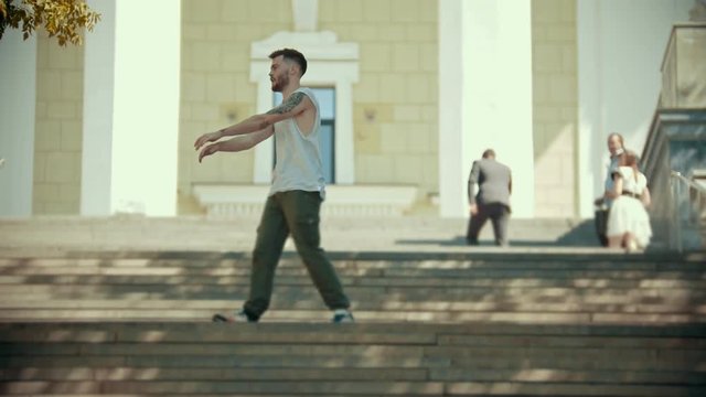 Young stylish happy man with tattoos dancing on the stairs on a background of a building