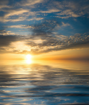 Sunset on the sea with reflection of clouds and the sun on the water surface.