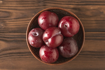Clay bowl with ripe plums on a wooden table. Flat lay.