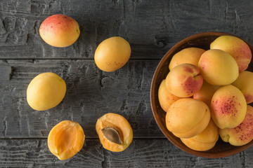 Bowl with big and ripe apricots on a wooden table.