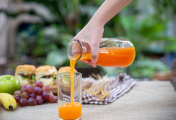 Pouring orange juice in the glass with breakfast background.