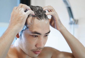 Fototapeta premium Closeup young man washing hair with with shampoo in the bathroom, vintage tone, selective focus