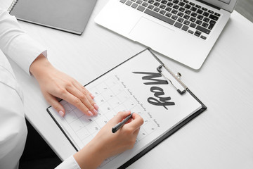 Young woman marking date in calendar at table, closeup