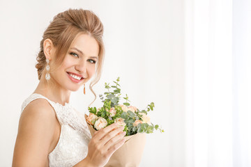 Beautiful young bride with bouquet of flowers near window