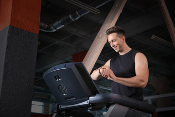 Fototapeta na wymiar Sporty young man with fitness tracker training on treadmill in gym