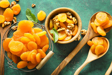 Bowl and spoons with dried apricots on color background