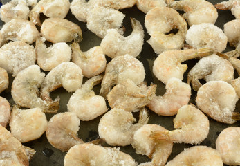 Frozen shrimp in shells thawing out on black cutting board