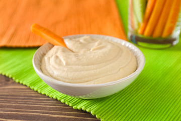 Bowl of tasty sauce and fresh carrot on wooden table
