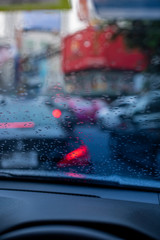 Rain drops on the windshield seeing from an interior of a car during a traffic jam in a peak hour in a big city during the day. Seeing car console as a foreground.