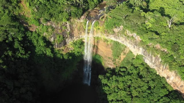  Aerial view of the amazing wonderful waterfall on the Mauritius island surrounded by tropical bushes and trees on a hot warm day. The concept of rest in natural reserves. 