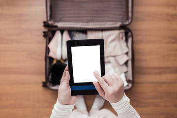 Top view of woman packing a luggage for a new journey. Female standing above suitcase with electronic note pad and cup of coffee. Space for text.
