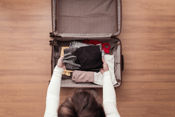 Top view of woman hands packing fitness clothing in a luggage (suitcase) for a new journey.