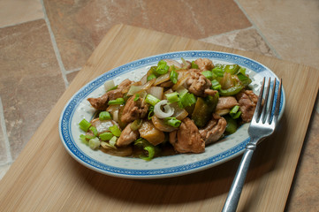 Oriental chicken with vegetables, onion, green pepers, and chopped chives on top, with a touch of soy sauce and ginger,.