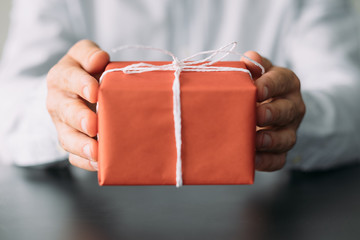 Office snacks delivery service. Closeup of red paper wrapped gift box in man hands. Copy space.