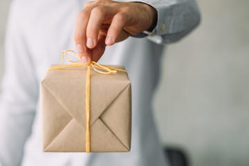 Goods delivery service. Closeup of beige gift box in business man hand. Copy space.