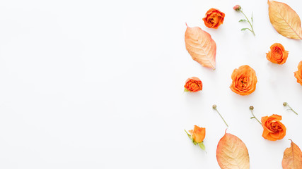 Autumn nature theme background. Red leaves and open orange rose buds scattered on white surface. Copy space.