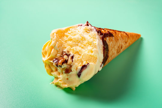 side view mango and chocolate flavor ice cream cone with couple of bites on green background - Powered by Adobe