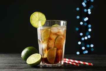 Glass of cold cola with citrus and ice on wooden table against dark background
