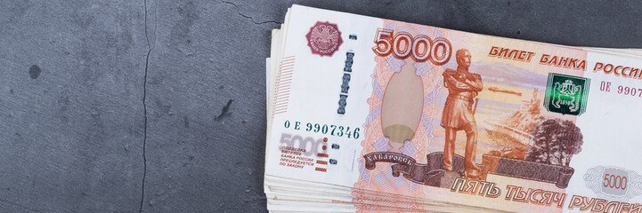 Big stack of Russian money banknotes of five thousand rubles lying on a grey cement background.