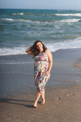 happy pregnant woman walking along sea shore