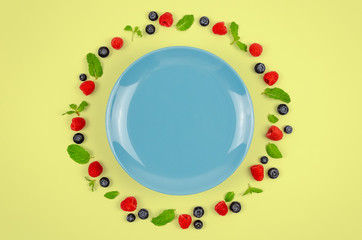 Fresh blueberries, raspberries and mint leaf on top view with blue plate and pastel yellow color background for healthy food concept. © baramyou0708