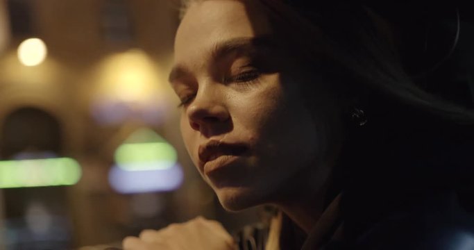 Young pretty girl in car, leans out passenger side car window, wind stirs her hair, she looks at the night city, night road, girl looking at the camera.