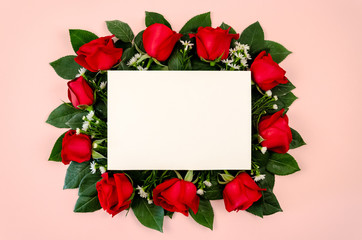 Red roses bouquet with blank white paper card on pastel pink background.